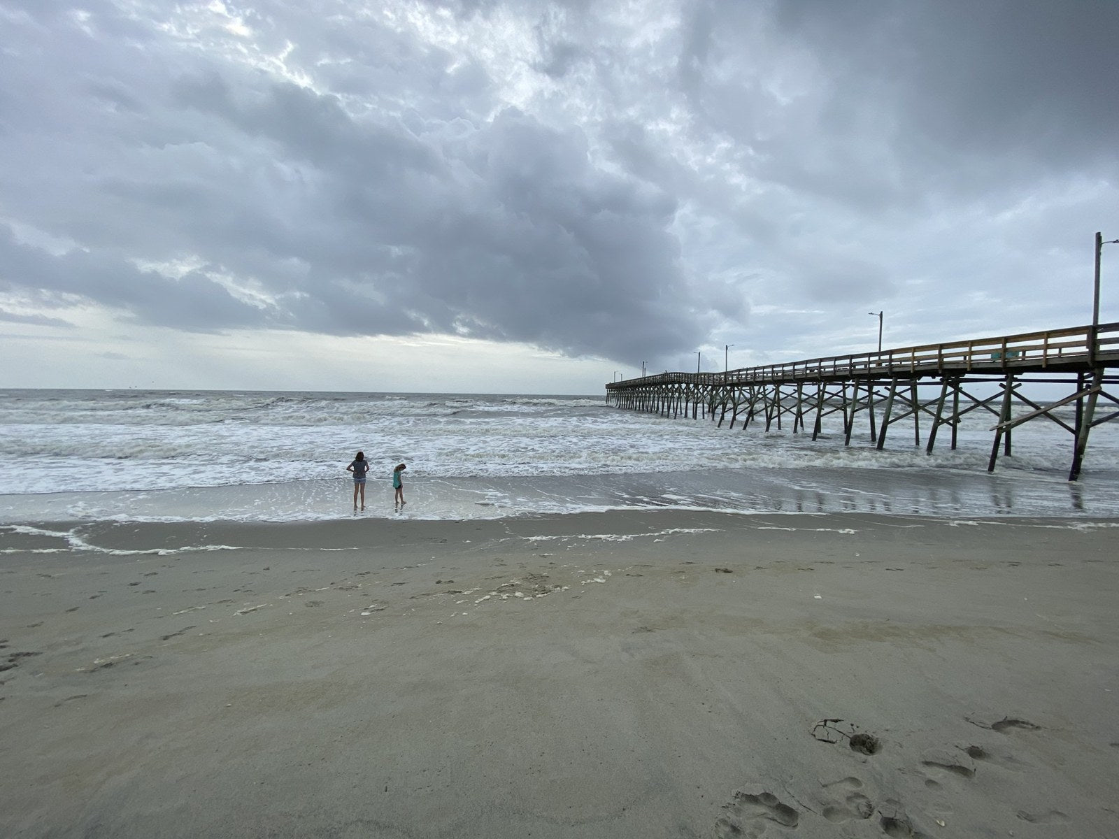 A fishing pier stretching over the surf beneath an overcast sky